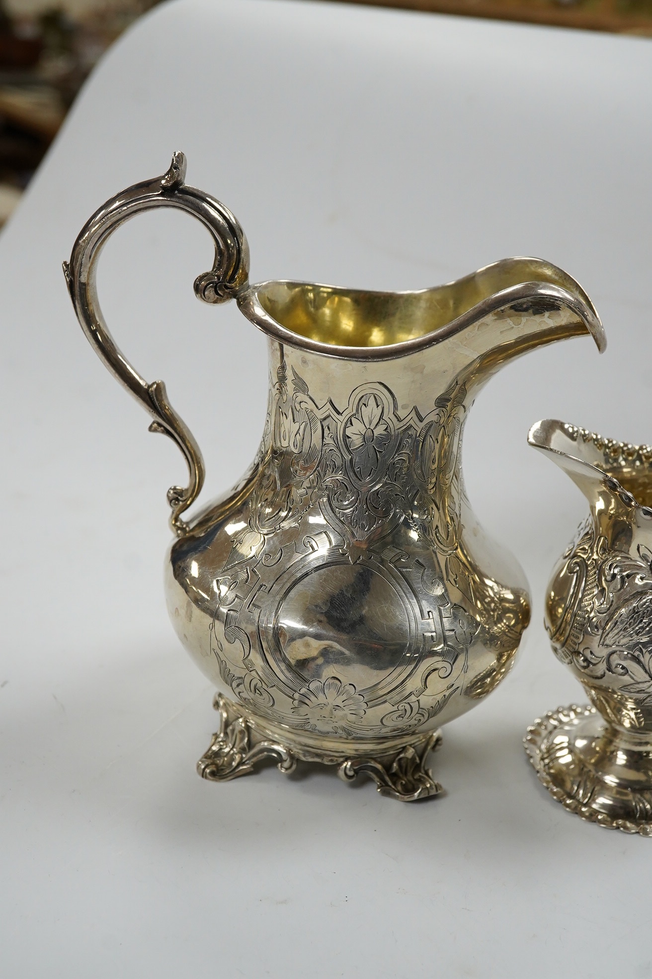 A Victorian engraved silver baluster cream jug, Henry Holland, London, 1862, 15cm, together with an Edwardian embossed silver cream jug, London, 1902, 10.5oz. Condition - poor